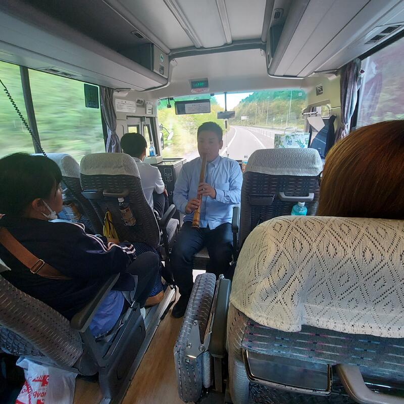 バスの中で尺八（５段）を披露する同窓会会長の平さん（H２７卒）